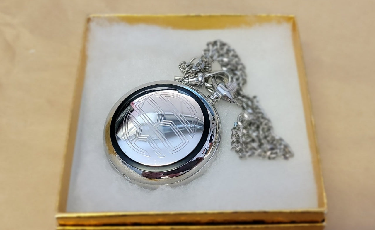 Engraved silver pocket watch with chain on a white cushion in a gold box
